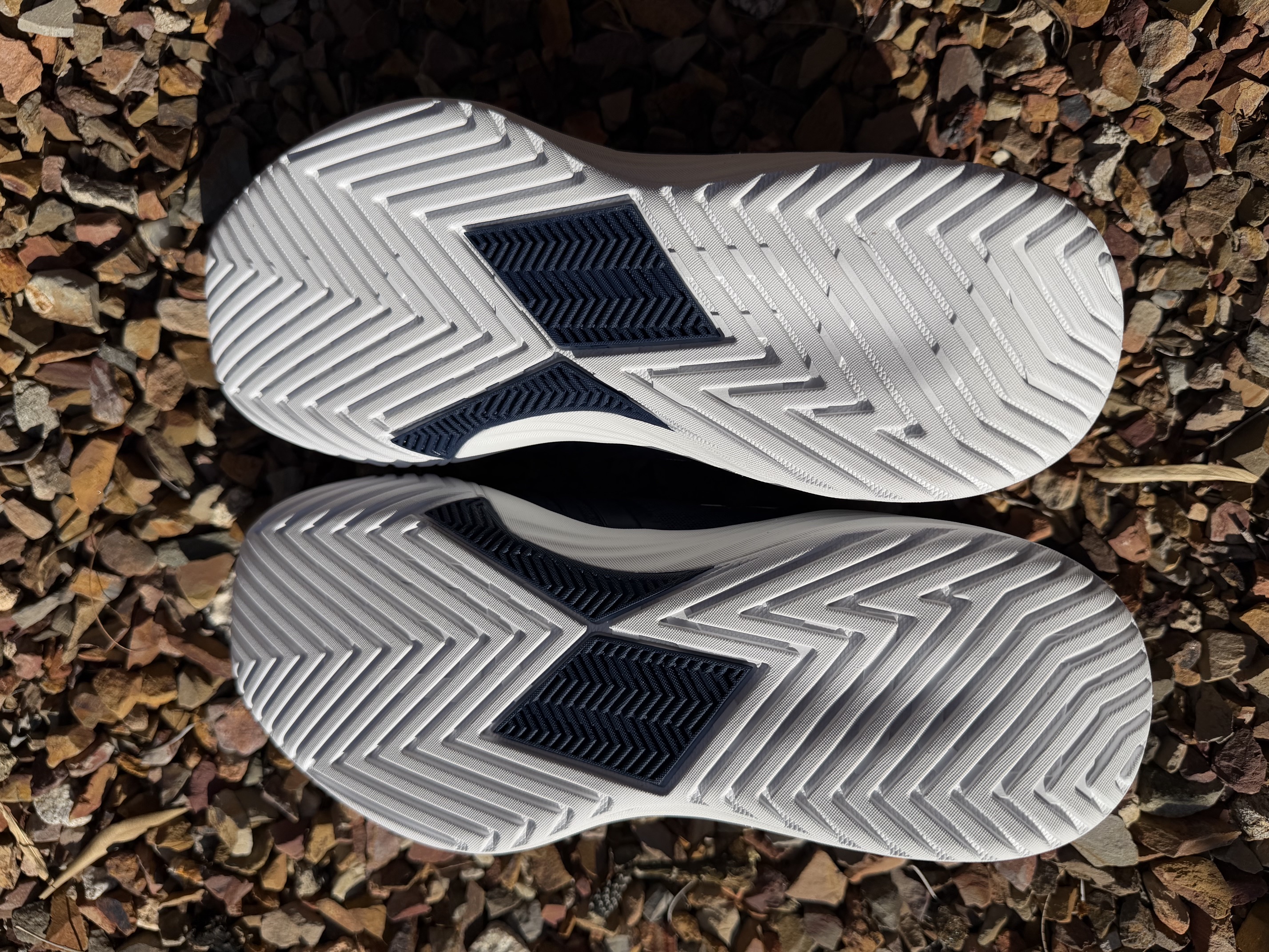 Outsole view of both Diadem Court Burst shoes showing the full-coverage herringbone tread pattern and the diamond-shaped pivot point at the medial forefoot.